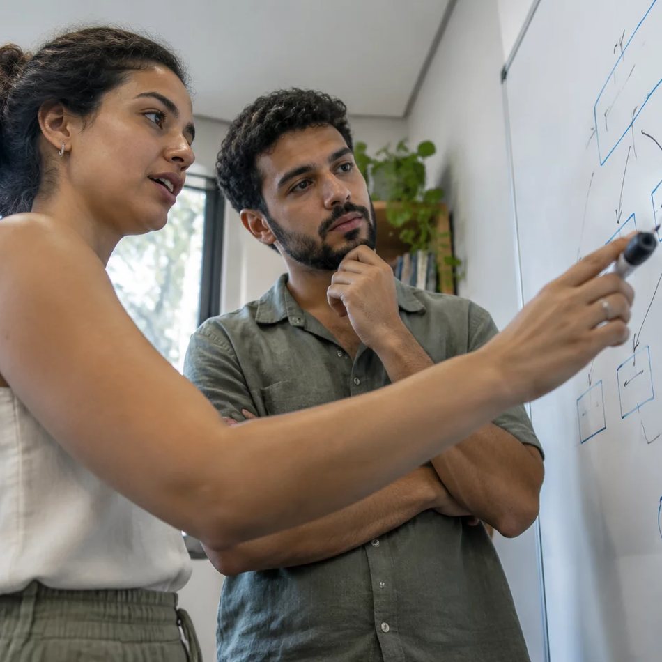Duas participantes de pé junto ao quadro branco, desenhando as partes de um argumento